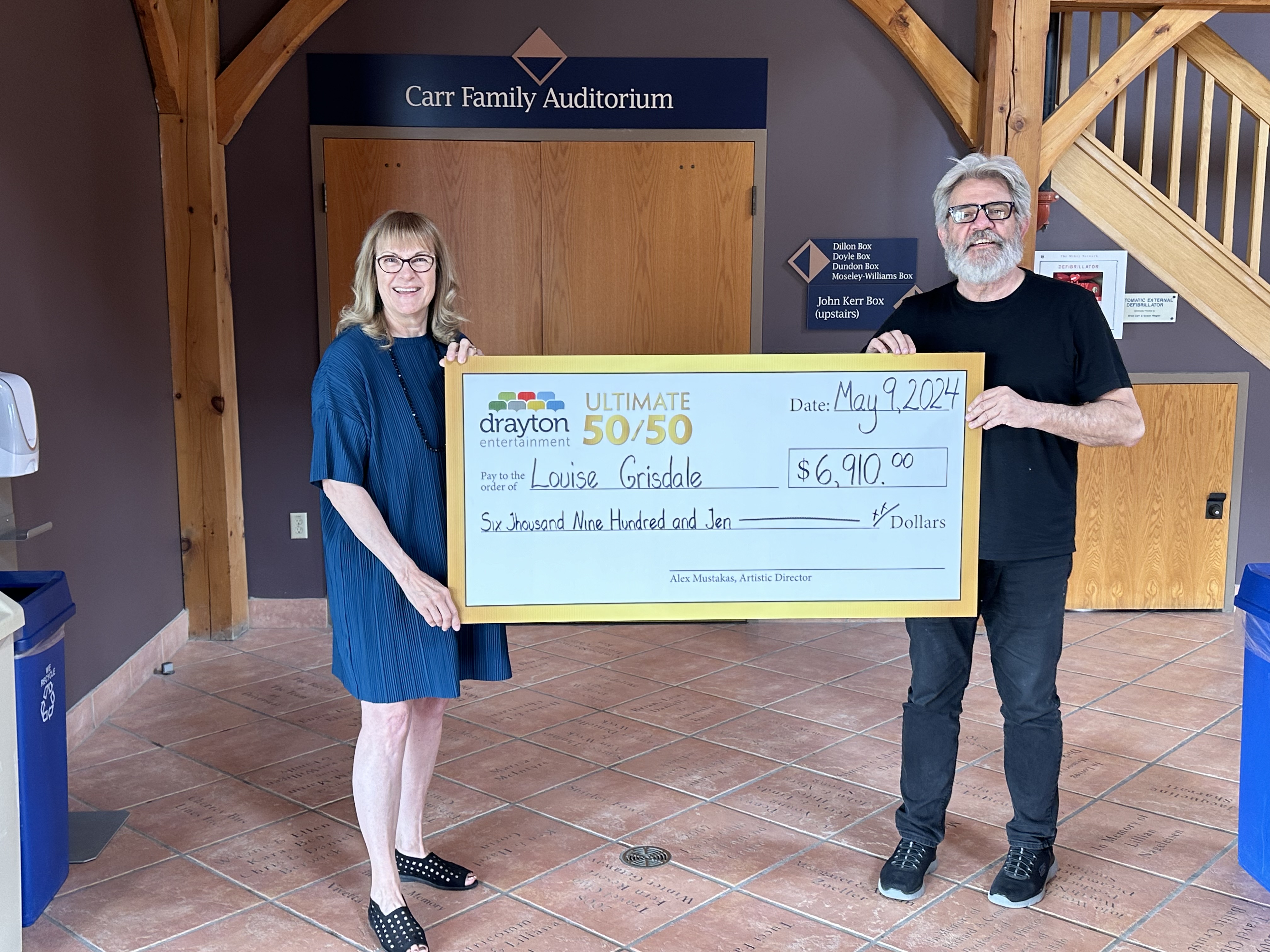 Marilyn Ivanovick and Gary Good hold a mock-up cheque in the foyer of Hamilton Family Theatre Cambridge